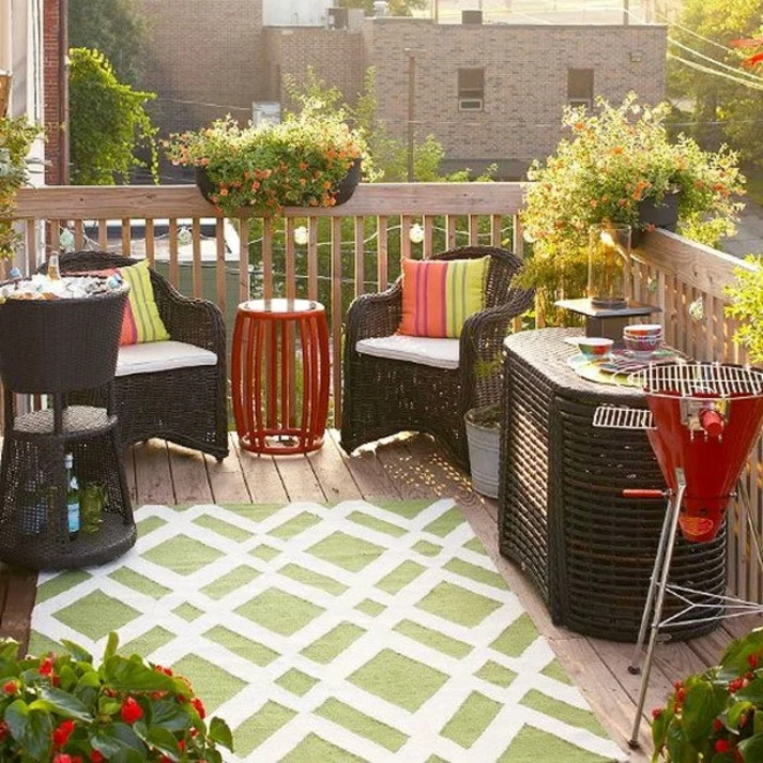 set of brown wicker furniture, two chairs and a table, wine cooler with ice, smaller red metal table, and grill in the same color, outdoor patio ideas, green and white rug and potted plants