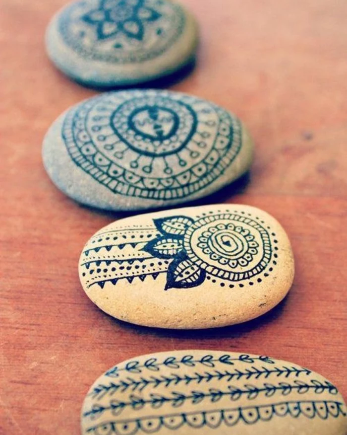 grey stones, decorated with black ink drawings, fun and easy crafts, showing mandalas and leaf patterns