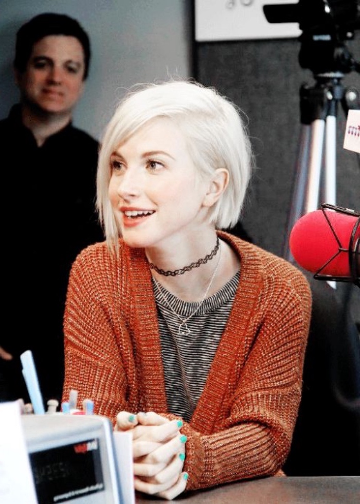 wayley williams sporting short platinum blond hair, with side parting, short bob haircuts, dark orange cable knit cardigan, and stripy top