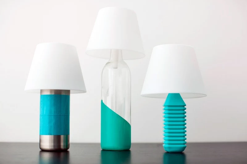 lamps made from three bottles, one silver colored with large blue stripe, one clear and partly dyed turquoise, and one plastic, fully died turquoise, with white lampshades