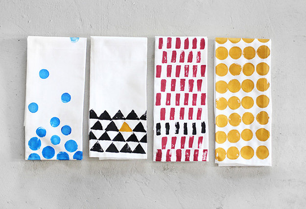 folded white napkins, a total of four, each decorated with a different stamped pattern, blue dots, black and yellow triangles, red and black rectangles, large yellow dots