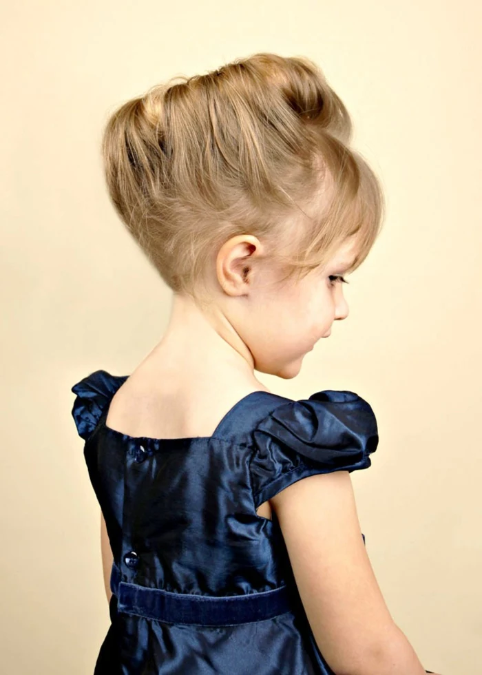 small blonde girl, with hair styled in renaissance-like hair bun, wearing a shiny, dark blue dress