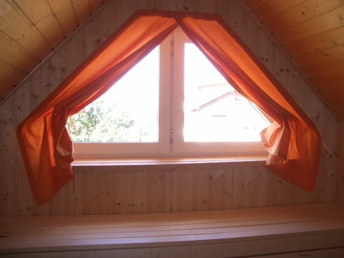 living room curtains ideas, close up of small attic window, surrounded by wooden paneling, decorated with orange red curtains