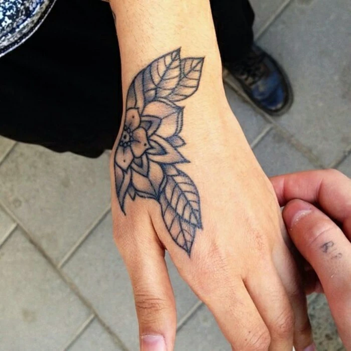lotus flower tattoo, close up of two hands, one has a simple shaded floral tattoo, done with black ink
