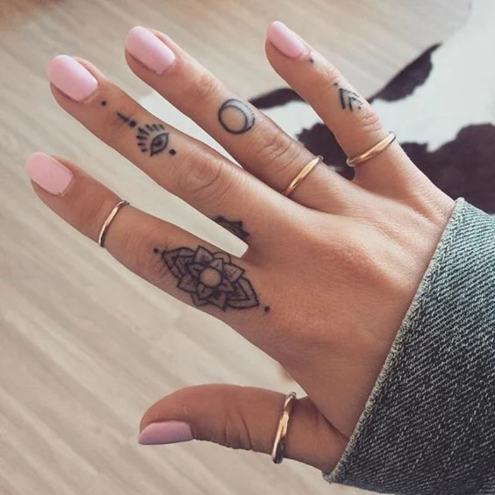 lotus flower tattoo, on a female hand's index finger, all-seeing eye tattoo on her middle finger, moon tattoo on her ring finger, small arrows tattoo on her little finger, pink nail polish, and simple golden rings