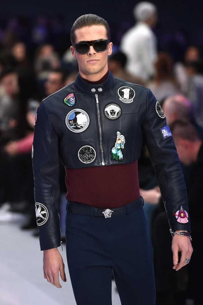 cropped black leather jacket with applique details, worn over maroon top, and skinny navy trousers, by man in dark sunglasses, 