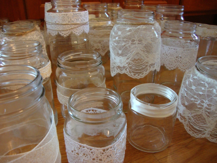 mason jar centerpieces, many differently shaped and sized jars, each decorated with white lace or ribbon, in a variety of patterns