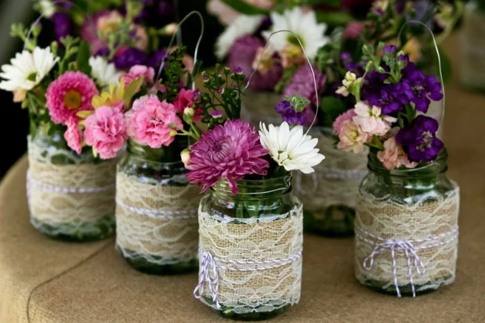 mason jar gifts, several jars with wire handles, decorated with lace over burlap, and two-toned string, containing white and yellow, pink and purple flowers