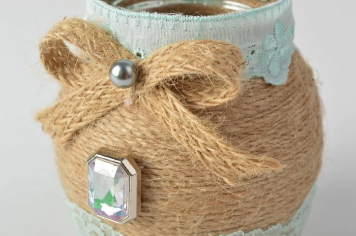 mason jar centerpieces, close up of small jar, decorated with woven string, pale blue ribbon, a silver pearl and a plastic gem