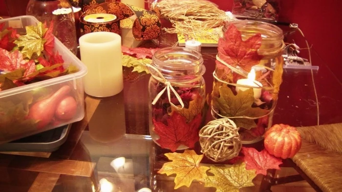 mason jar decorations, two differently sized jars, decorated with autumn leaves in orange and yellow, with candles and leaves, small pumpkins and gourds nearby