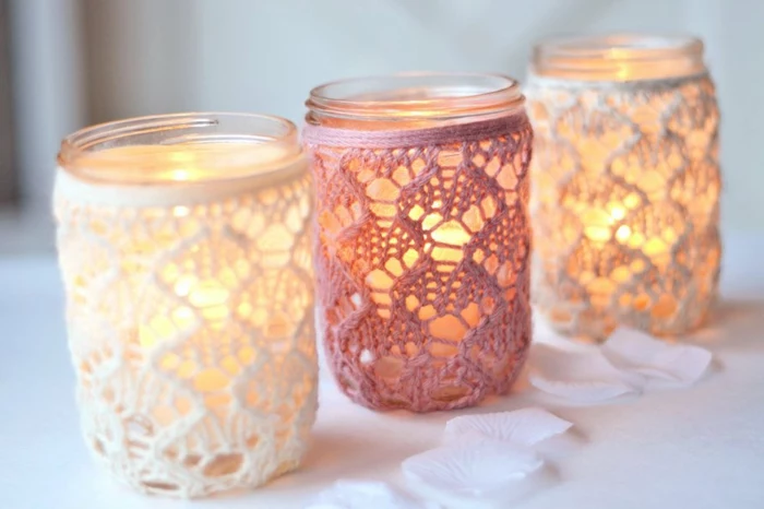 mason jar centerpieces, three jars lit from within, two decorated with white lace, one with pink, white rose petals nearby