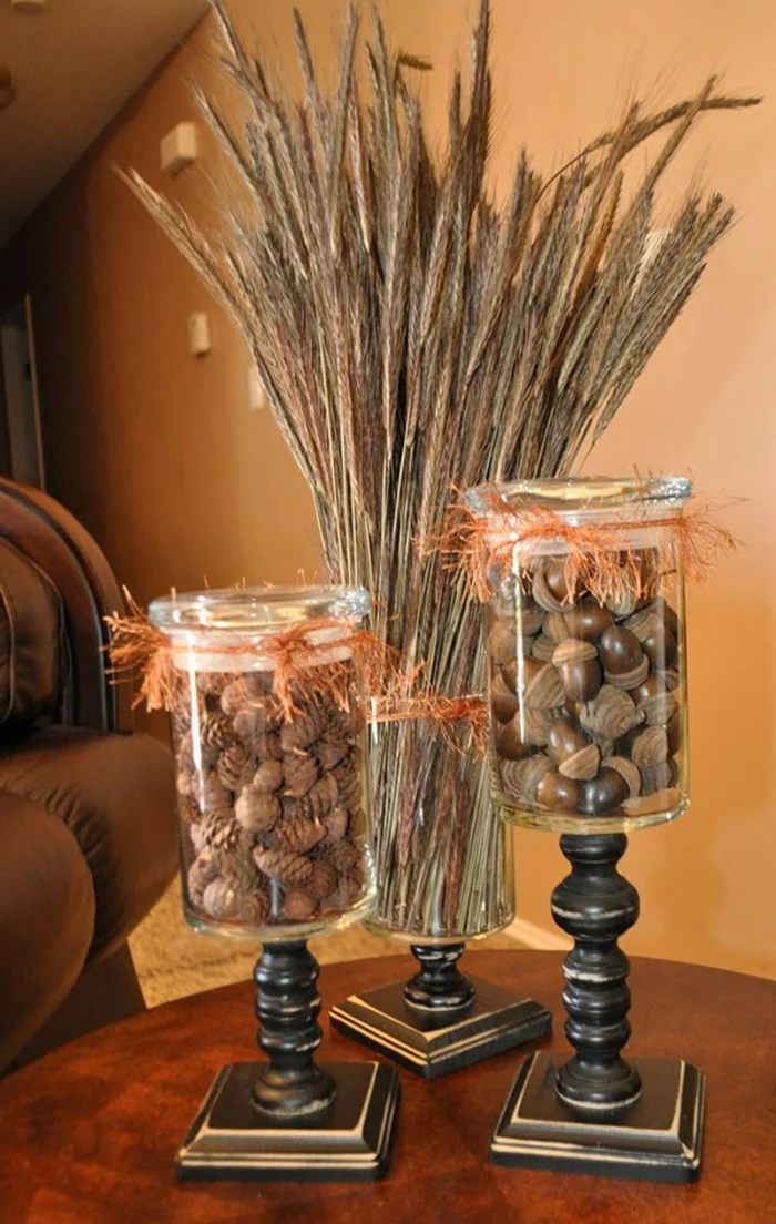 decorating mason jars, three clear jars, stuck to vintage wooden stands, containing tiny fir cones, acorns or a bunch of dried wheat stalks