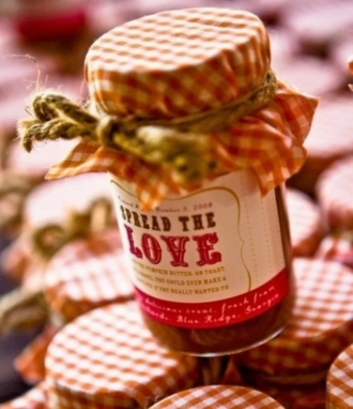 diy mason jar, close up of jar filled with red substance, covered in red and white checkered cloth, tied with a string, with a label saying spread the love, placed on top of many similar jars