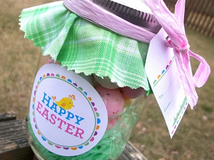 diy mason jar, with a round colorful label reading happy easter, covered with green and white plaid cloth, and containing colorful candy and easter grass