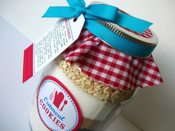 diy mason jar, clear jar filled with layers of ingredients, with a round label reading oatmeal cookies, covered with a red and white checkered cloth, and a teal ribbon