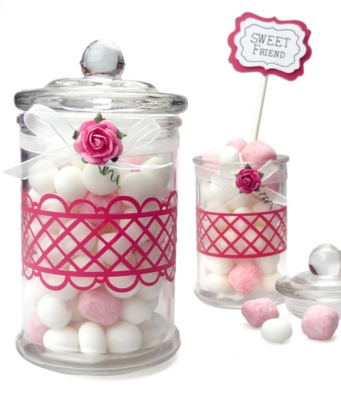 mason jar crafts, two clear jars with glass lids, filled with white and pink candy, decorated with pink details, white ribbons with bows, and tiny pink roses