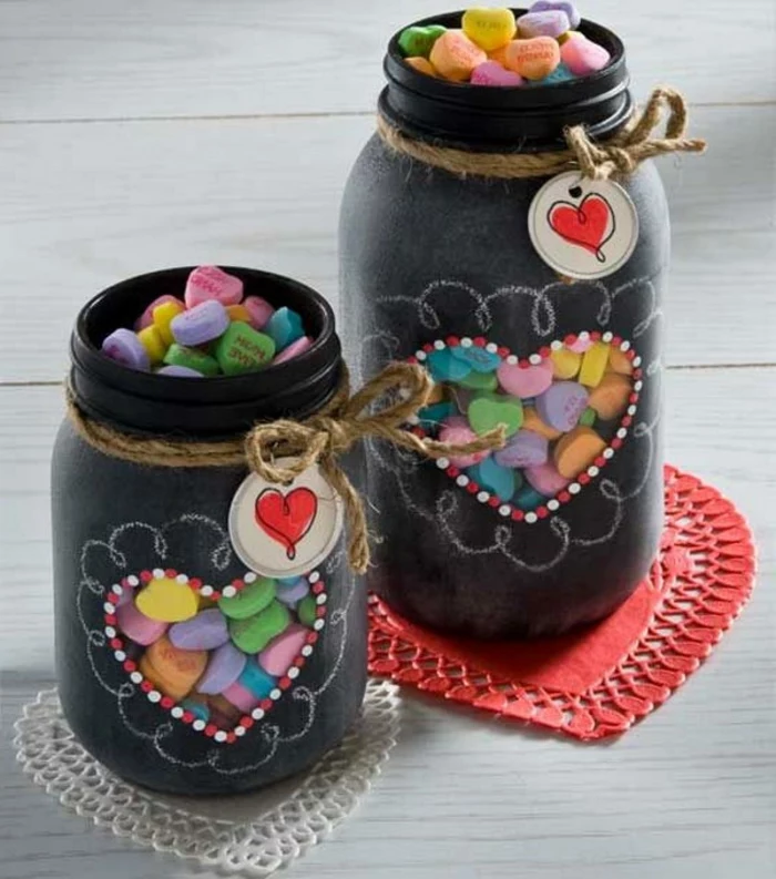 two differently sized jars, painted in black matte color, and decorated with white chalk, with heart-shaped windows, revealing colorful candy inside