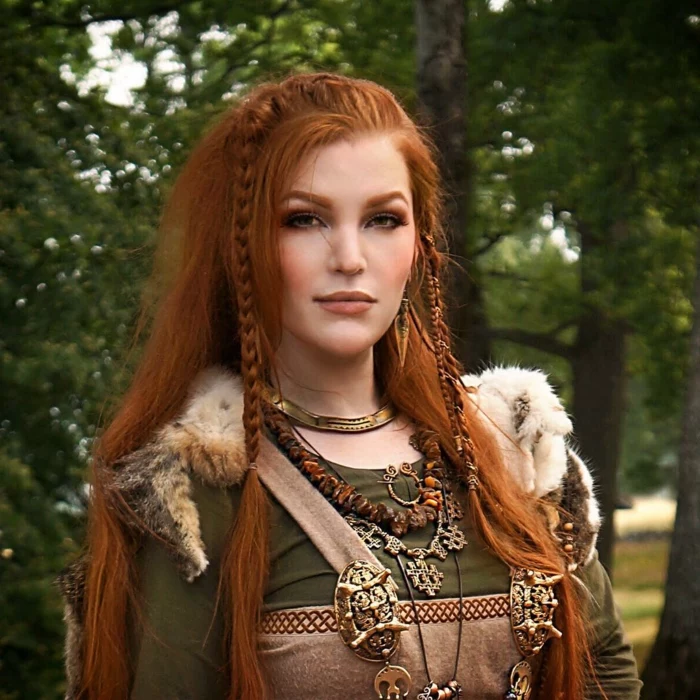 medieval braids, red-haired woman, long hair decorated with two braids, wearing a green and pale brown dress, with a fur cape, jewelry and ornaments from gold, amber and silver
