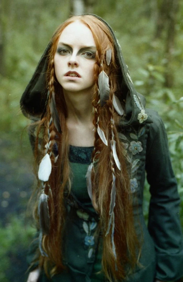medieval braids, young woman wearing green embroidered dress with hood, long ginger hair, decorated with several braids, and many feathers, strong green eye makeup, renaissance braided hairstyles