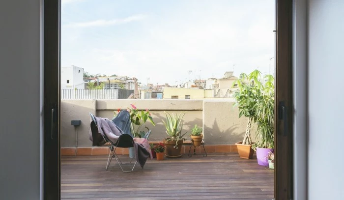 large minimalist terrace, with a single lounging chair, covered by several blankets, few different potted plants in pink, orange and green pots nearby