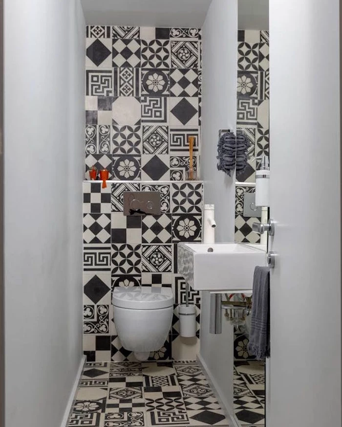 bathroom remodels, narrow toilet with two white walls, third wall and floor are covered in black and white, mismatched and patterned tiles, rectangular white sink and plain toilet bowl