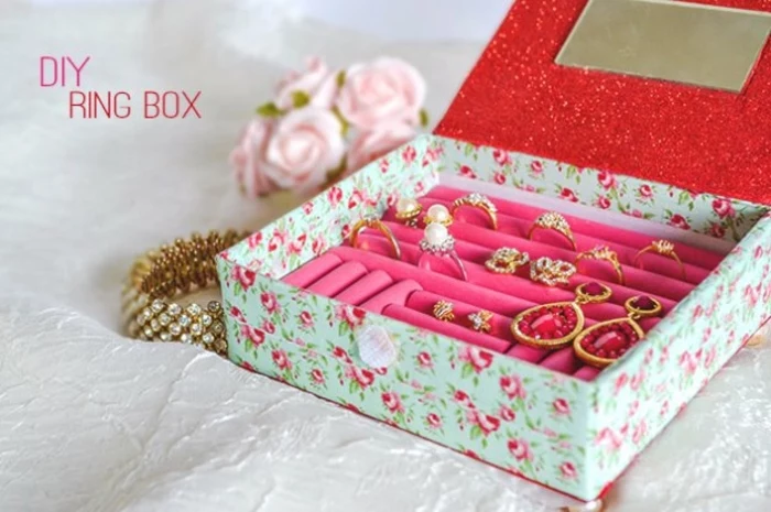 jewelry box in pale blue, with rose pattern outside, and pink and red inside, easy arts and crafts, various rings and earrings inside, barcelet and pink roses nearby
