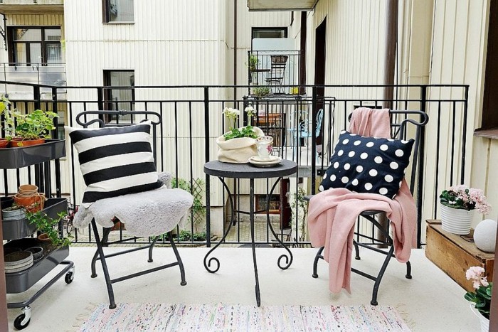 small round black metal table, and two matching chairs, each covered with a different throw and cushion, with shelves containing potted flowers nearby, front porch decorating ideas