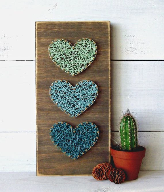 rectangular wooden board, decorated with three heartshapes, made with nails, and string in different shades of blue, easy arts and crafts, cactus plant nearby