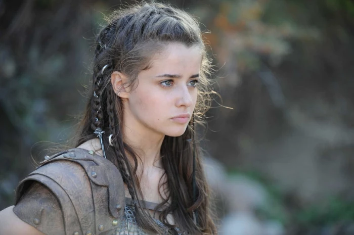 teenage girl wearing knight-like armor, with messy brown hair, decorated with two small braids, and silver ornaments