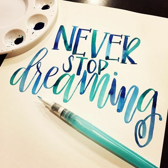 white sheet of paper, with the words never stop dreaming, written in blue watercolor, palette with blue paint, and marker-like brush nearby, homemade crafts