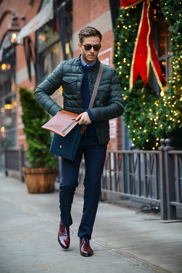 warm puffy down jacket in black, worn by young man in smart navy trousers, business casual dress code, with dark blue jumper, brown leather shoes, and brown and navy bag