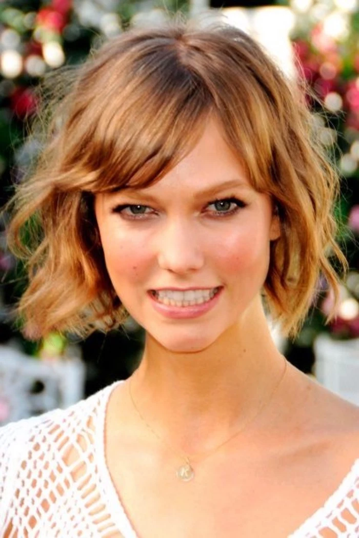 karlie kloss with curly, copper colored short bob, and side bangs, wearing white meshy top