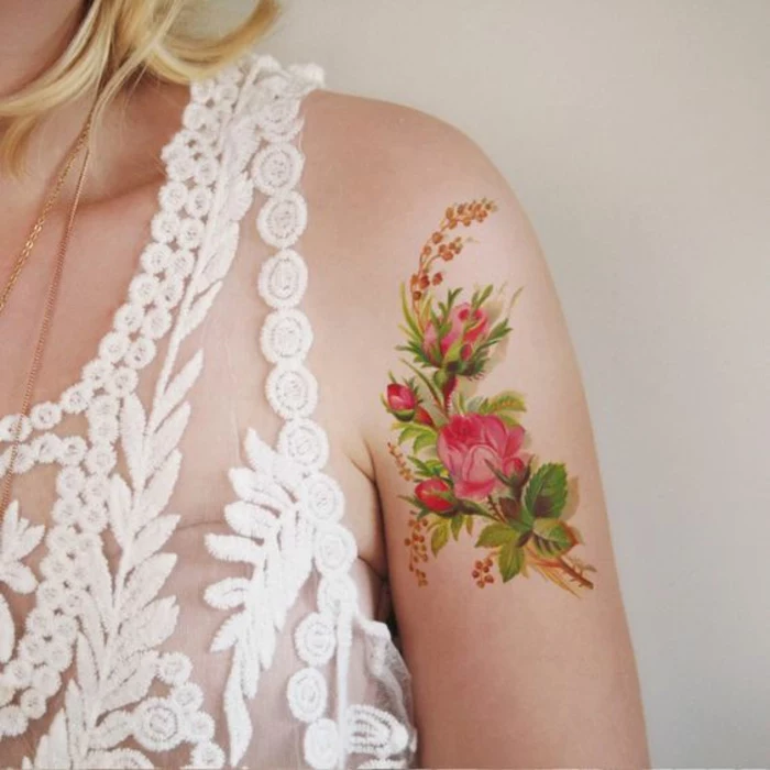 shoulder flower tattoos, blonde woman with sheer, white embroidered dress, a tattoo of several pink roses, with green leaves and other smaller plants, near her shoulder