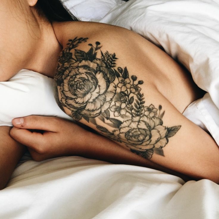 shoulder flower tattoos, brunette woman, half covered in white duvet, elaborate floral tattoo, of peonies and other small flowers and leaves, done in black ink