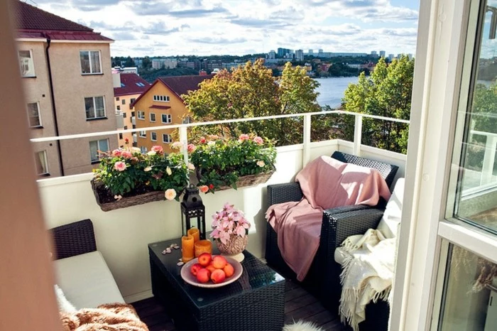 porch décor, black table with candles, fruit and flowers, near black cozy chairs, with white and pink blankets, near potted plants, lovely town view