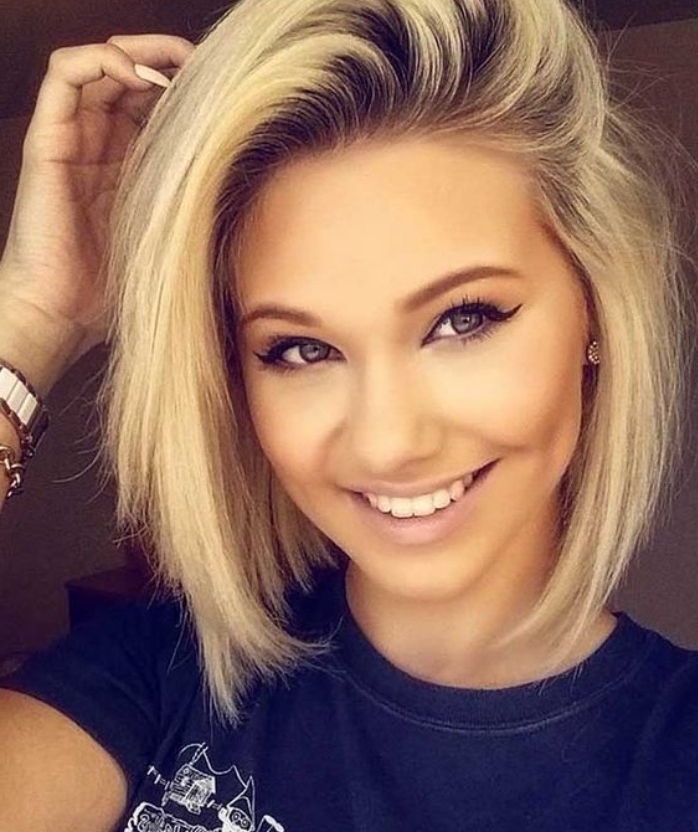 smiling woman with nude colored lipstick, and black eyeliner and mascara, wearing side-swept blond bob, with dark roots