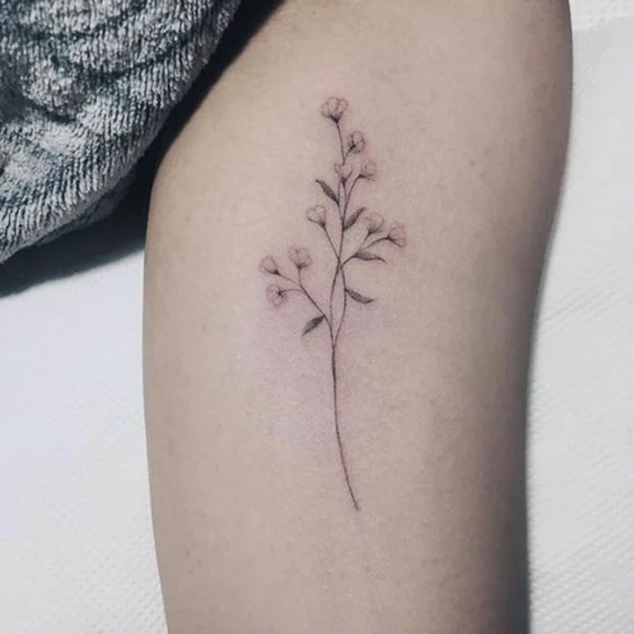 minimalist tattoo of a thin, delicate plant with small petals and leaves, done with black ink, on a woman's thigh