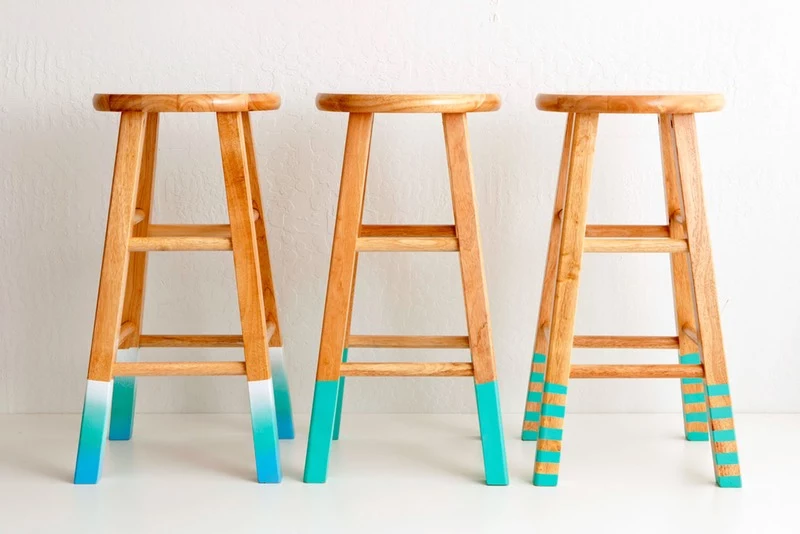three bar stools, the tips of their legs have been painted, one in white and teal with ombre effect, one plain turquoise, one striped turquoise