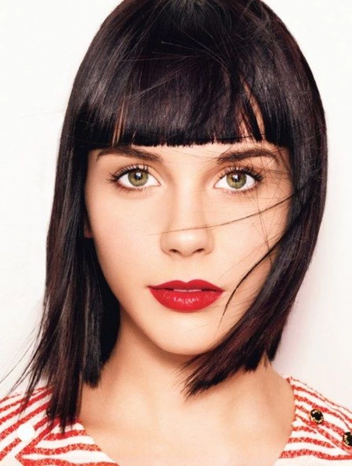 dark smooth and straight hair, with even bangs, worn by woman with hazel eyes, and vivid red lipstick