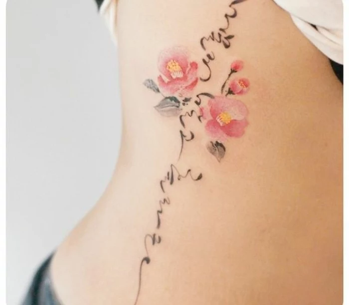 two pink cherry blossoms, with two pink buds, and three pale green leaves, surrounded by black calligraphy strokes, tattooed on the side of a person's stomach