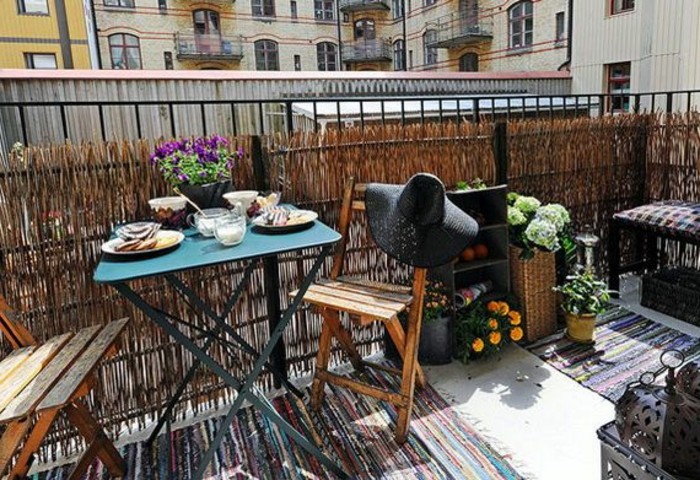 teal-blue-metal-table-set-for-breakfast-with-purple-flowers-in-black-pot-two-wooden-garden-chairs-one-decorated-with-big-black-straw-hat-and-multicolored-rug-porch-ideas blue metal table set for breakfast, two wooden chairs, one decorated with black straw hat, flowers an house plants, front porch décor
