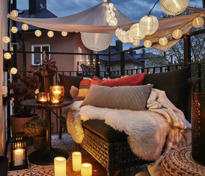 brown settee with pillows, throws and blankets, near small round black table, with many lit candles, covered patio ideas, baldachin with many lit lanterns overhead
