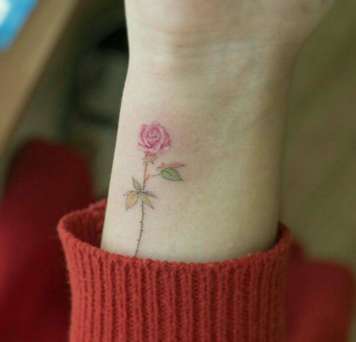 traditional flower tattoo, small pale tattoo, of a pink rose, with brown stalk, and yellow-green-leaves, on a person's arm, near their wrist
