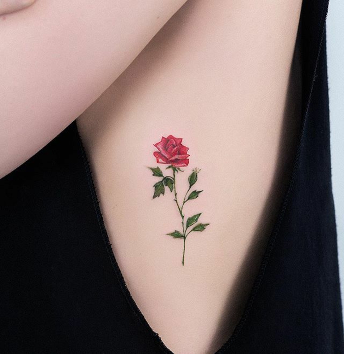 botanical tattoo, of a realistic rose, with red petals and green stalk and leaves, on a person's side