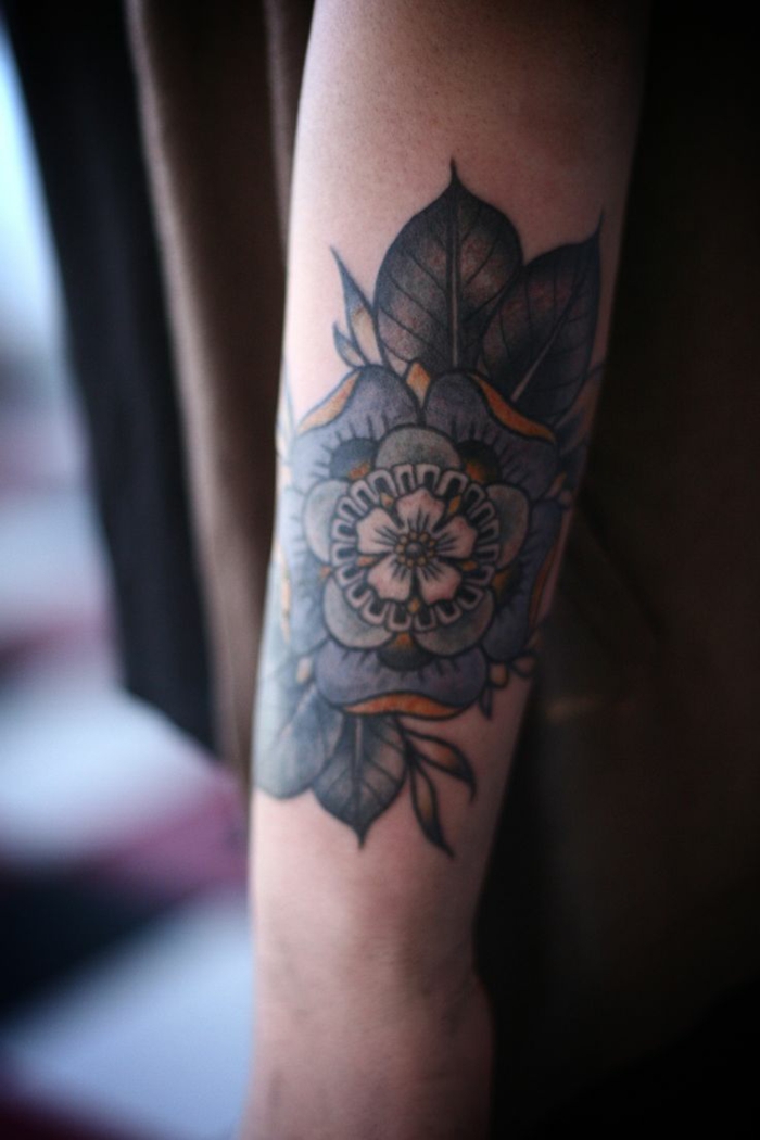 close up of an elaborate floral tattoo, with several rows of petals, in white and blue, with yellow details, and several green leaves