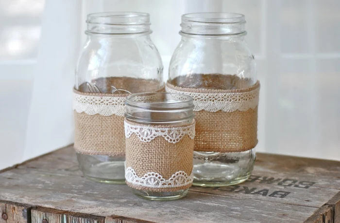 decorating mason jars, two large and one small jar, with beige burlap and white lace, placed on an overturned wooden crate