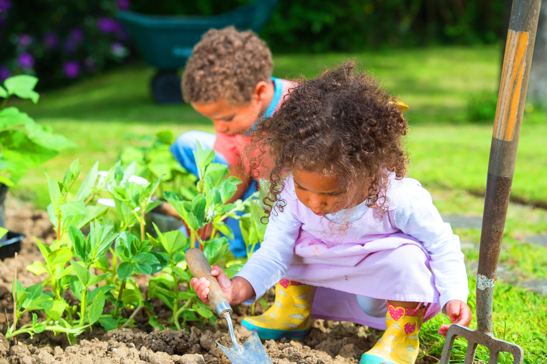 two small children, a boy and a girl, gardening near green plants