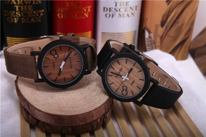 wooden detail wristwatches, one with a brown strap, and one with a black strap, placed on wooden stands, near several books