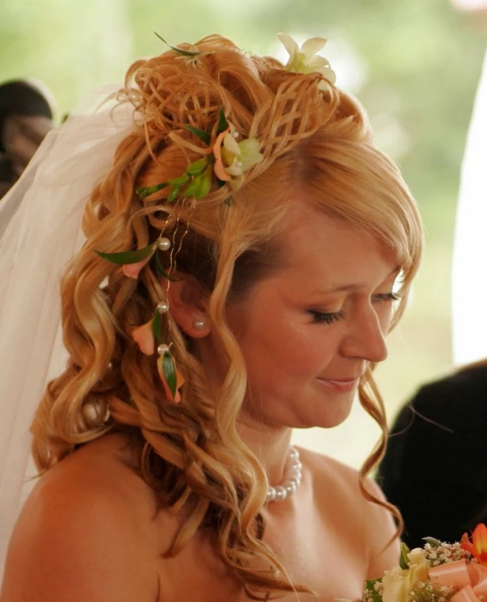 middle age hairstyles, smiling bride with white veil, blonde hair falling in lose curls, with a tiara made from twisted hair strands, decorated with pearls, pink and white flowers