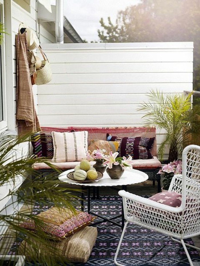 settee with four multicolored cushions, near white round table, and white chair, front porch décor, with patterned rug and potted plants